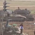 Израильский солдат, стоя на бронетехнике, развернул израильский флаг с цветами Л…